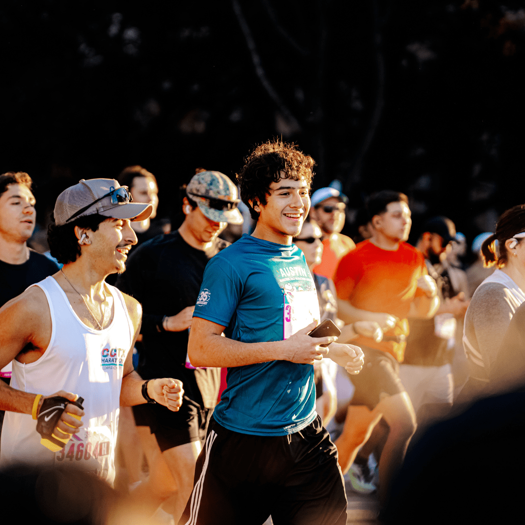 A group of people run outdoors in the Austin Marathon, with two young men in the foreground smiling and wearing athletic gear and race bibs, surrounded by other runners in sunlight, capturing the excitement of Austin Marathon history. Austin Marathon Half Marathon & 5K A group of people run outdoors in the Austin Marathon, with two young men in the foreground smiling and wearing athletic gear and race bibs, surrounded by other runners in sunlight, capturing the excitement of Austin Marathon history. Austin Marathon Half Marathon & 5K