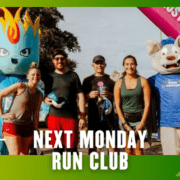 A group of five smiling runners and a blue mascot pose at a colorful outdoor event finish line, celebrating their Group Run. Text reads, "Next Monday Run Club" at the bottom of the image. Austin Marathon Half Marathon & 5K