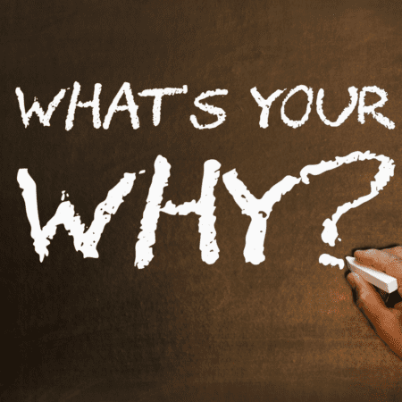 A hand holding chalk writes “WHAT’S YOUR WHY?” in bold white letters on a dark brown chalkboard—a reminder to find your Running Motivation and overcome the Post-Race Blues. Austin Marathon Half Marathon & 5K