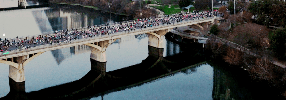 A large crowd of runners crosses a bridge in downtown Austin, Texas, with the city skyline in the background. The image highlights the 2026 Austin Marathon’s 35th anniversary for use in the official Austin Marathon media guide. Austin Marathon Half Marathon & 5K
