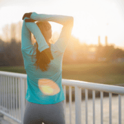 A person in athletic clothing stretches their arms overhead while standing on a bridge at sunrise, embodying the energy needed when motivation fades. The sun shines brightly in the background as they face away from the camera. Austin Marathon Half Marathon & 5K