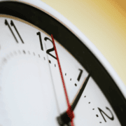 Close-up of a wall clock showing the time as 11:59, with the second hand near the 12. The clock face is white with black numbers, and the image is slightly tilted—serving as a timely reminder about running safety and how important it is to train safely, especially when every minute counts. Austin Marathon Half Marathon & 5K