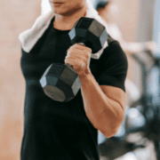 A person in a black shirt holds a dumbbell in one hand and has a white towel draped over their neck, working out in a gym, embodying top productivity tips for effective time management and February planning. Austin Marathon Half Marathon & 5K