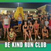 A group of people of various ages pose together outdoors at night in South Austin, dressed in athletic wear, with a banner at the bottom that reads “Be Kind Run Club.” It’s clear this group run is part of the local Rise and Run community spirit. Austin Marathon Half Marathon & 5K