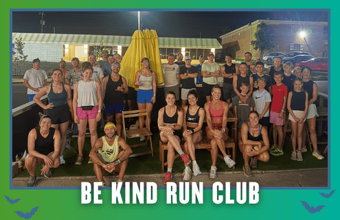 A group of people of various ages pose together outdoors at night in South Austin, dressed in athletic wear, with a banner at the bottom that reads “Be Kind Run Club.” It’s clear this group run is part of the local Rise and Run community spirit. Austin Marathon Half Marathon & 5K