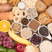 An assortment of healthy foods including fruits, beans, grains, bread, pasta, seeds, sweet potato slices, and nuts arranged on a wooden surface—ideal choices for marathon fuelings and gut training during marathon training. Austin Marathon Half Marathon & 5K