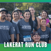 A group of smiling people wearing “Lakerat Run Club” shirts pose together outdoors at a South Austin running event during KickOff Week, with trees in the background and race numbers visible, celebrating their group run. Austin Marathon Half Marathon & 5K