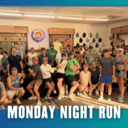 A group of people in athletic wear pose together indoors, smiling and ready for a group run. Text at the bottom reads āMonday Night Run.ā The background displays hats and clothing on the walls, hinting at the community spirit of Lakerat Run Club as they celebrate KickOff Week. Austin Marathon Half Marathon & 5K