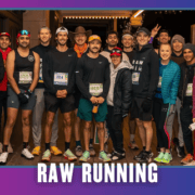 A group of runners in athletic gear pose together and smile at night on a city street under the text āRAW RUNNING.ā Representing Latinas Run ATX, some wear hats and race bibs; a few flash peace signs, celebrating the spirit of a vibrant group run. Austin Marathon Half Marathon & 5K
