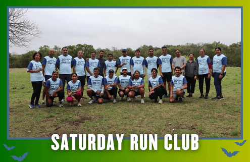 A group of runners in matching shirts pose outdoors on grass, smiling for a photo under cloudy skies during KickOff Week. The image has a border with “Saturday Run Club” written at the bottom, capturing the spirit of this lively Group Run. Austin Marathon Half Marathon & 5K
