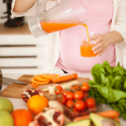 A person pours orange juice into a glass next to a cutting board with sliced oranges, carrots, and fresh vegetables including tomatoes, spinach, and apples—perfect ingredients for marathon fueling or gut training during marathon training. Austin Marathon Half Marathon & 5K
