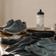 Running gear on a wooden table, including blue sneakers, stacked socks, a water bottle, black waist pouch, sport watch, light green cap, and teal athletic clothing under natural light—your essential Running Checklist for a seamless Training Upgrade. Austin Marathon Half Marathon & 5K