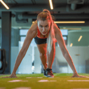 Athletic woman in sportswear crouches at a starting line indoors, preparing to sprint with intense focus and hands on the ground—demonstrating the dedication found in essential workouts that build marathon longevity. Austin Marathon Half Marathon & 5K