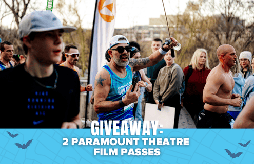 A group of runners at an outdoor event, with one man in sunglasses and a blue tank top cheering. Text on a blue banner reads: “GIVEAWAY: Win tickets—2 Paramount Theatre Film Passes.”. Austin Marathon Half Marathon & 5K