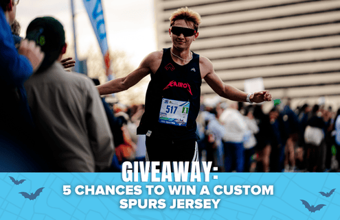 A runner in sunglasses finishes a race with arms outstretched. Text overlay reads: “GIVEAWAY: 5 CHANCES TO WIN A CUSTOM SPURS JERSEY AND YETI COOLER.” Crowd and buildings are visible in the background. Austin Marathon Half Marathon & 5K