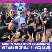 A group of marathon runners in Team SPIbelt shirts pose for a photo with an Austin Marathon mascot while wearing race medals. Text overlay reads: “Austin Marathon celebrates 20 years of SPIbelt at 2027 event.” Austin Marathon Half Marathon & 5K