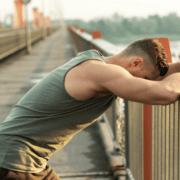 An exhausted man in a green tank top leans against a bridge railing, taking a moment for exercise recovery. Austin Marathon Half Marathon & 5K